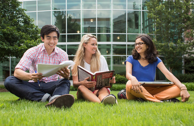 students sitting in the grass reviewing books