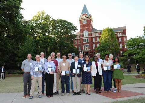 Faculty and staff honorees hold their awards during a group photo in front of Tech Tower 